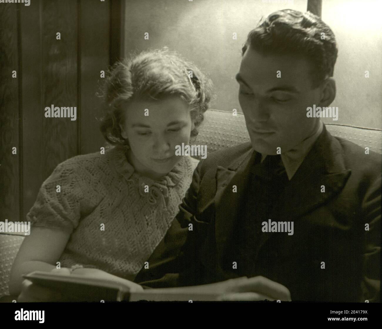 Una coppia condivide un momento intimo leggendo un libro insieme negli anni trenta Foto Stock