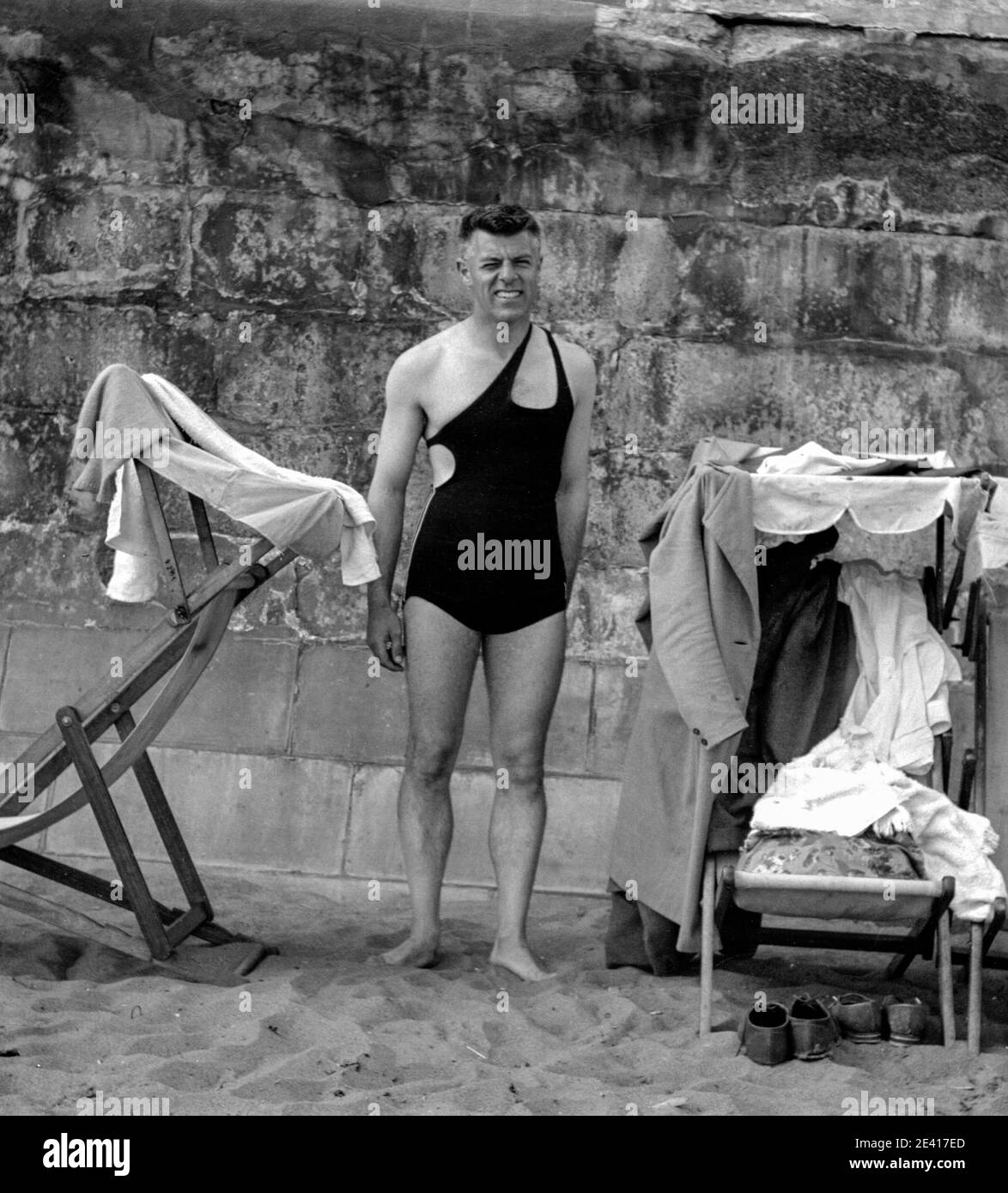 Un uomo si pone di fronte al muro di mare Il suo costume da bagno nero a pezzo unico su una spiaggia inglese negli anni trenta Foto Stock