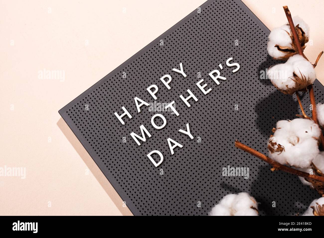 Tavola di plastica grigia con citazioni bianche Happy Mother's Day e ramo di cotone su sfondo beige. Foto Stock