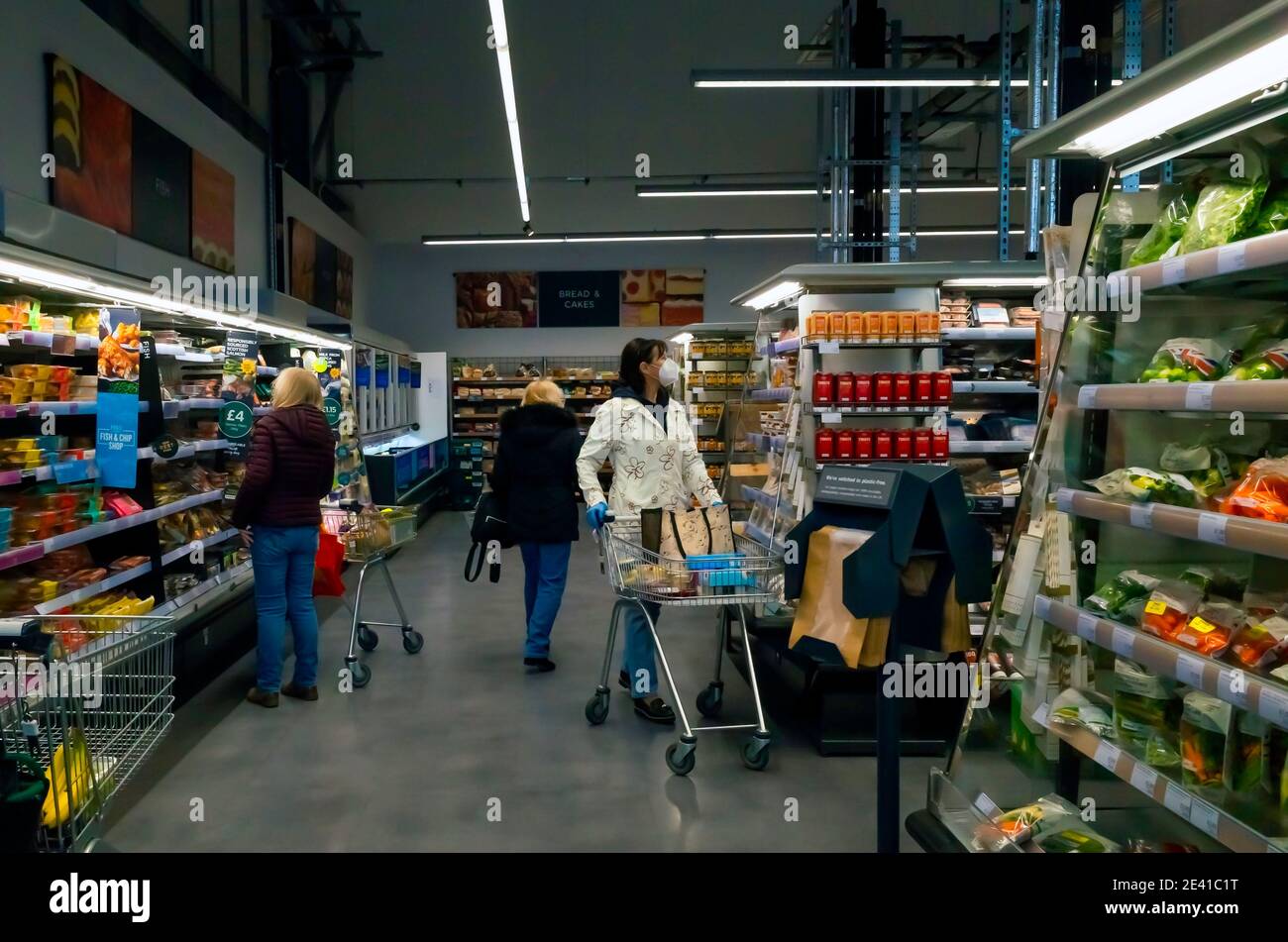 Esposizione supermercato di scaffali ben riforniti di cibi cotti surgelati frutta e verdura con tre donne che acquistano Foto Stock