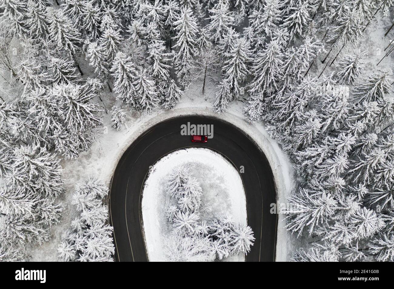 Vista aerea sulla strada nella foresta con una macchina in inverno. Paesaggio invernale con alti pini coperti di neve. Foto Stock
