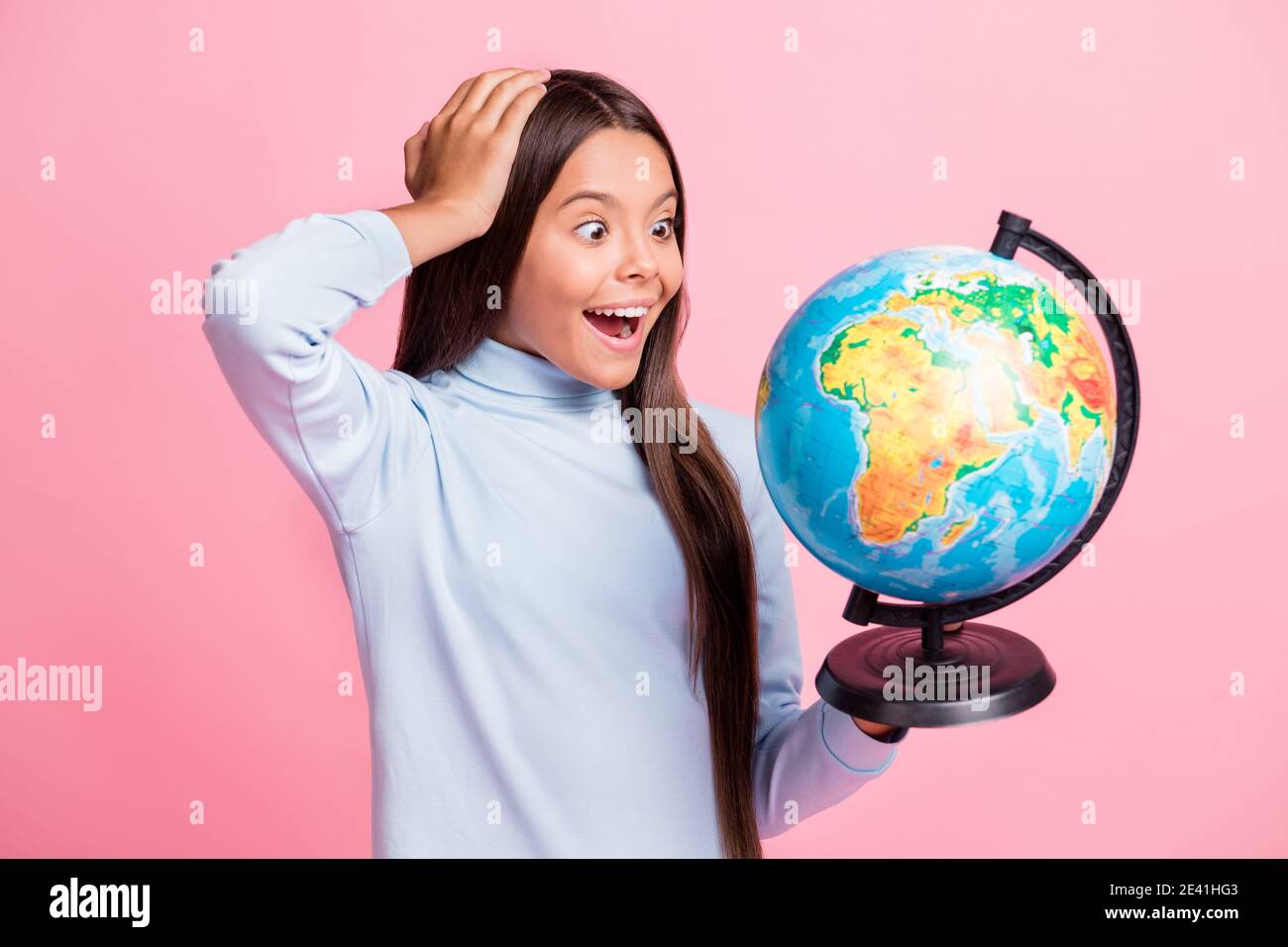 Primo piano ritratto di bella allegra ragazza stupita che tiene nelle mani i paesi di apprendimento del globo lezioni isolate su sfondo di colore pastello rosa Foto Stock