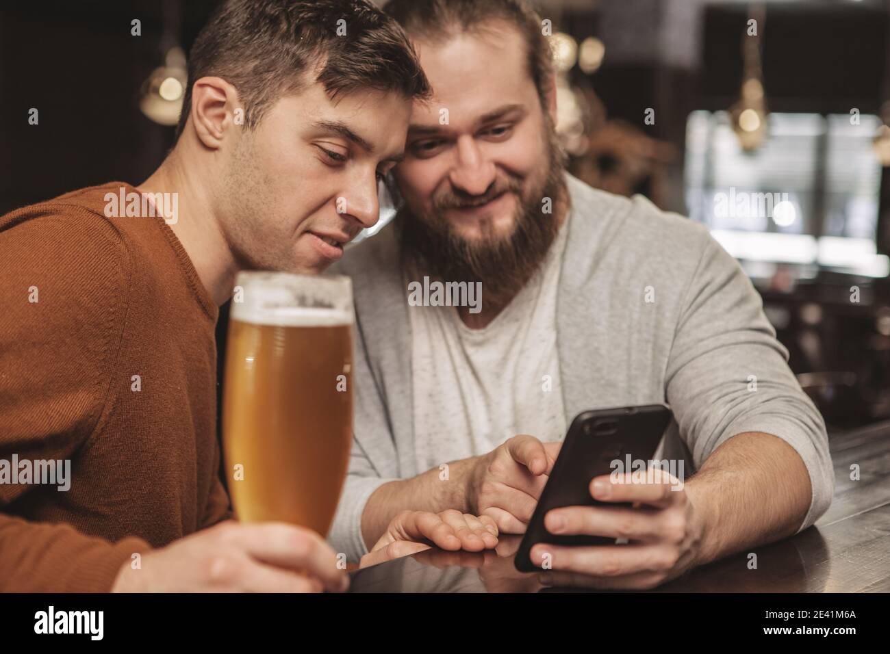 Due amici maschi che si divertono a riposarsi insieme al pub della birra, a guardare le notizie online, utilizzando lo smartphone. Uomo bearded che naviga su Internet, mostrando som Foto Stock