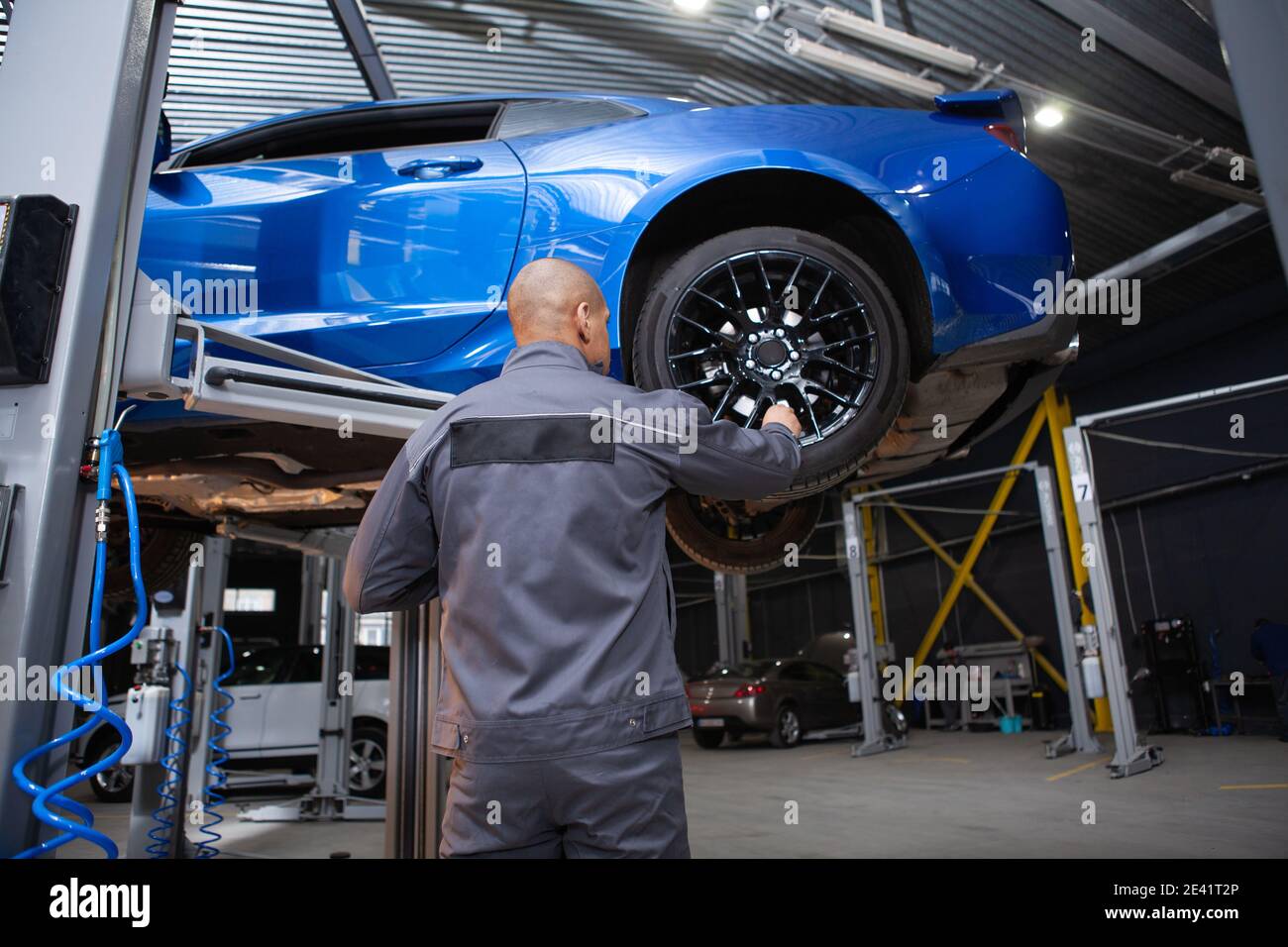 Vista posteriore a basso angolo di un addetto alla manutenzione di un'automobile che esamina l'automobile sollevata, spazio di copia Foto Stock