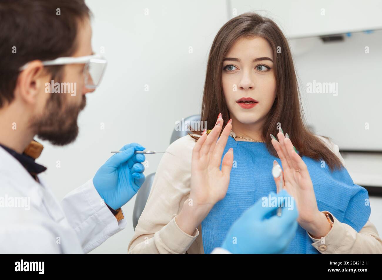 Giovane donna che guarda spaventato e nervoso seduto in sedia dentale di fronte al suo dentista. Terrorizzata donna paura del trattamento dentale Foto Stock