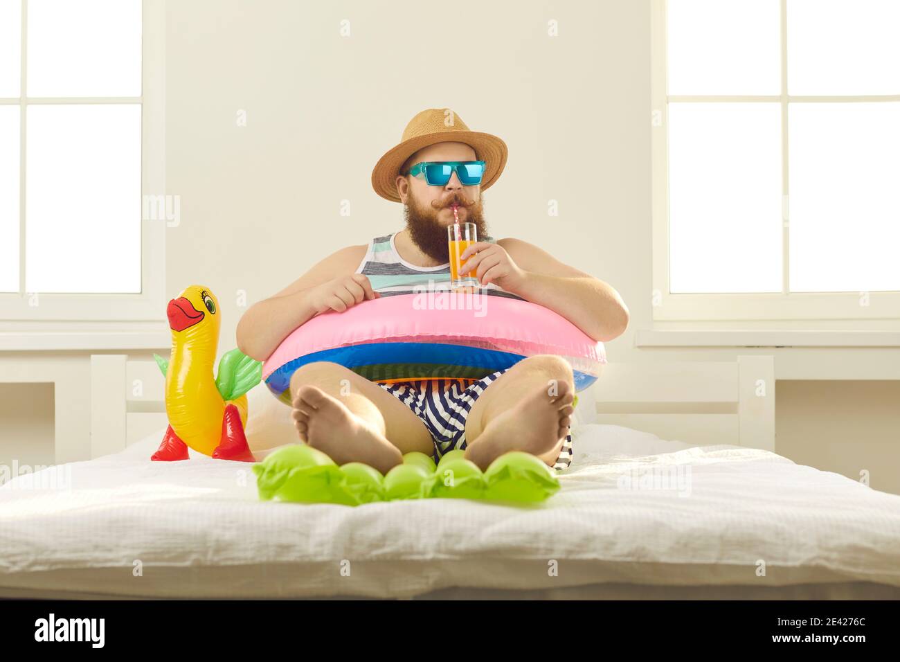 Divertente giovane uomo a piedi nudi in estate indossare sorseggiando cocktail sulla spiaggia in quarantena a casa Foto Stock