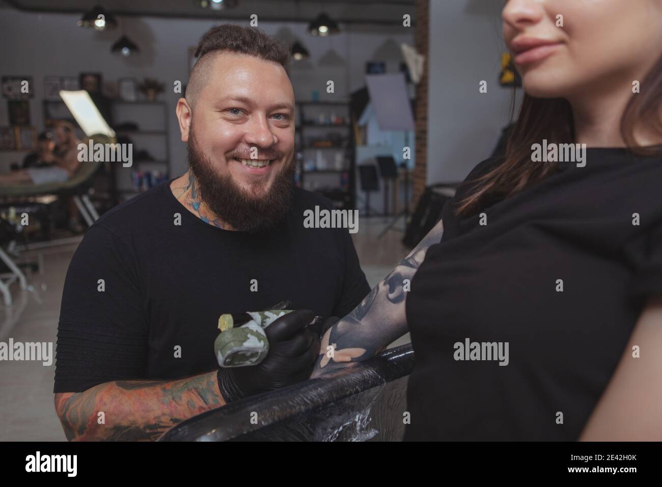 Ripresa di un felice artista di tatuaggio maschile bearded sorridente, lavorando su un tatuaggio manica a braccio su una cliente femminile Foto Stock