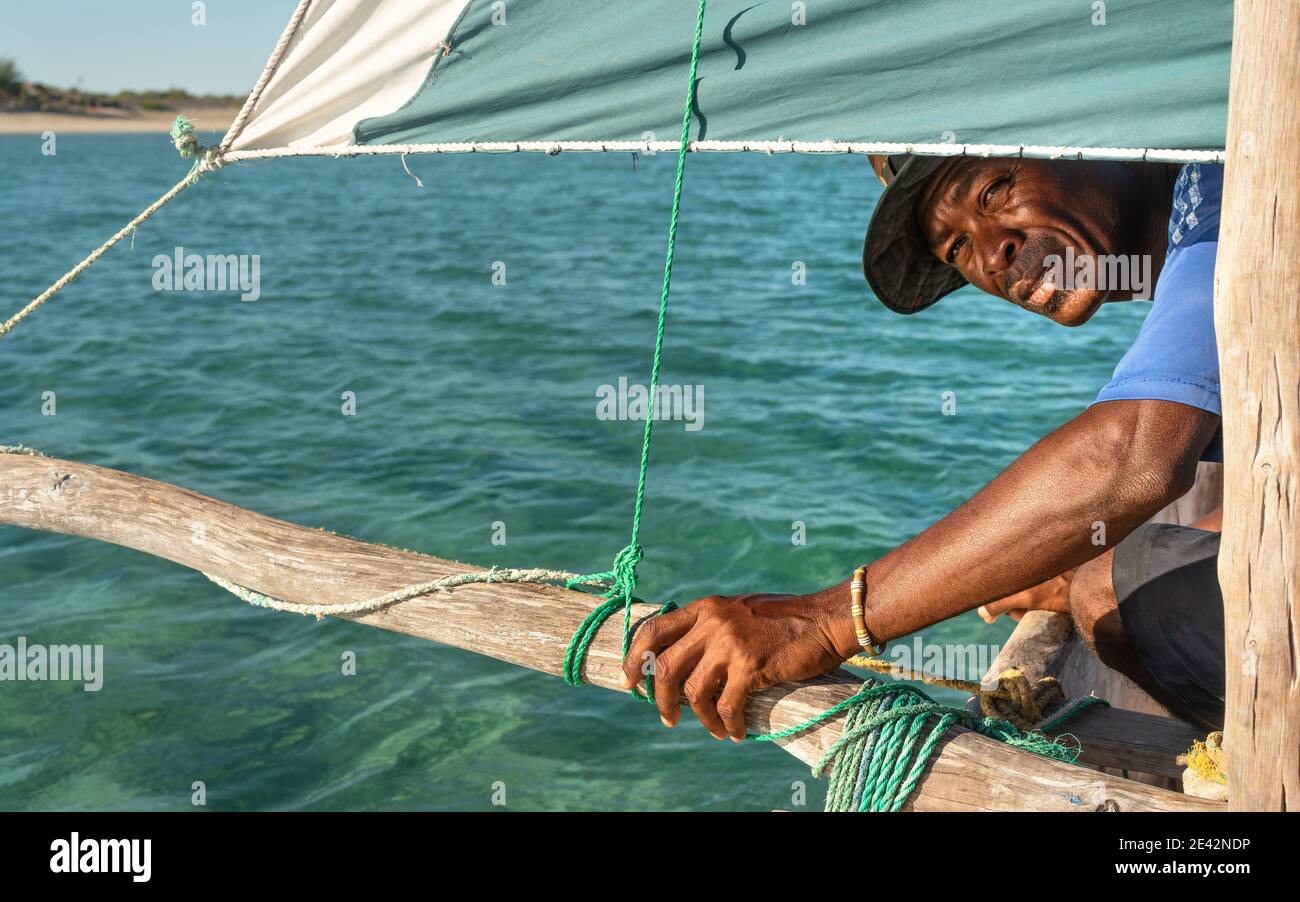 Anakao, Madagascar - 03 maggio 2019: Sconosciuto pescatore malgascio guardando indietro sotto la principale vela verde della sua piroga (piccola barca da pesca), verde blu mare du Foto Stock