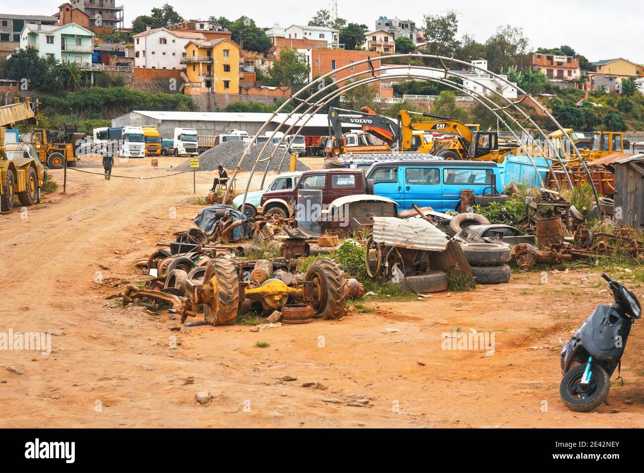 Antananarivo, Madagascar - 24 aprile 2019: Varie parti di automobili su terra di polvere rossa di piccolo cantiere vicino alla strada principale, camion e vehi di costruzione Foto Stock