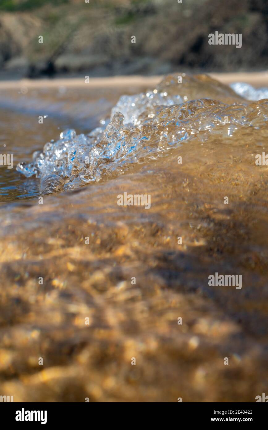 Onde che si infrangono sulla costa, spray, acqua bianca e luce riflessa sulla superficie dell'acqua Foto Stock