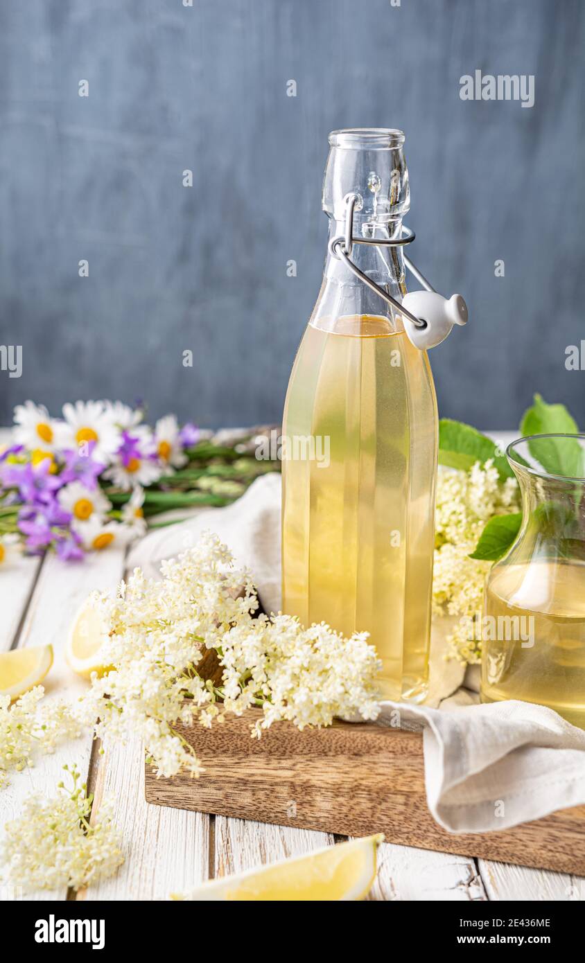 Deliziosa bevanda rinfrescante sana, sciroppo dolce di fiori di sambuco o cordiale in una bottiglia di vetro su rustico sfondo di legno Foto Stock