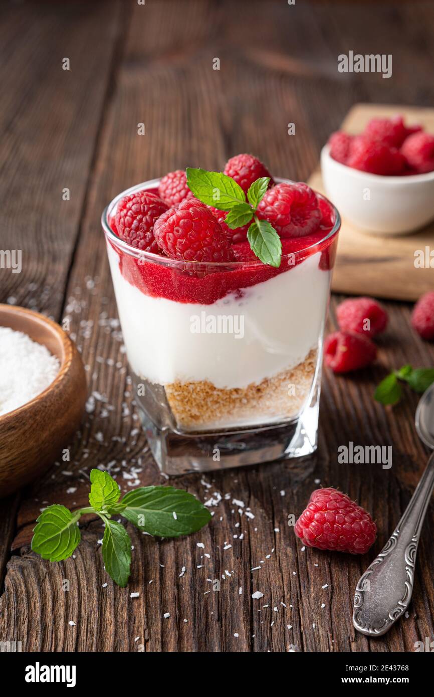 Non cuocere il dessert alla cheesecake in un recipiente di vetro con il coperchio purea di lamponi e bacche fresche su rustico sfondo di legno Foto Stock