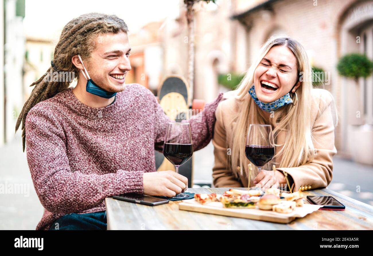 Giovane coppia in amore indossare maschera viso aperto divertirsi Al wine bar esterno - felici amanti moderni che trascorrono il pranzo insieme al ristorante dehor Foto Stock