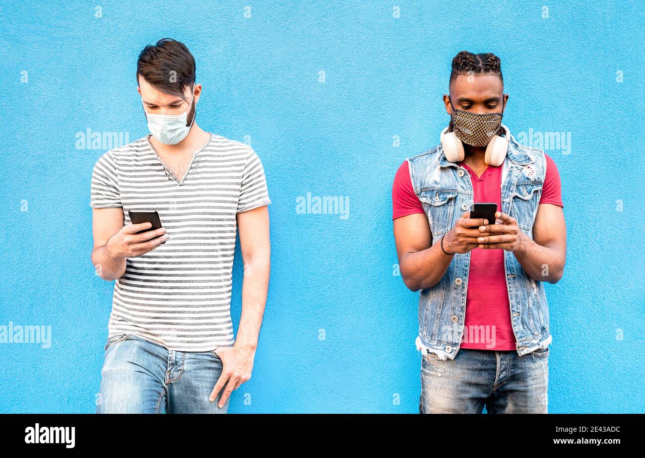 Amici maschili multirazziali con maschere facciali utilizzando l'app Tracking con Smartphone - giovani milleniali che guardano gli aggiornamenti su social network Foto Stock