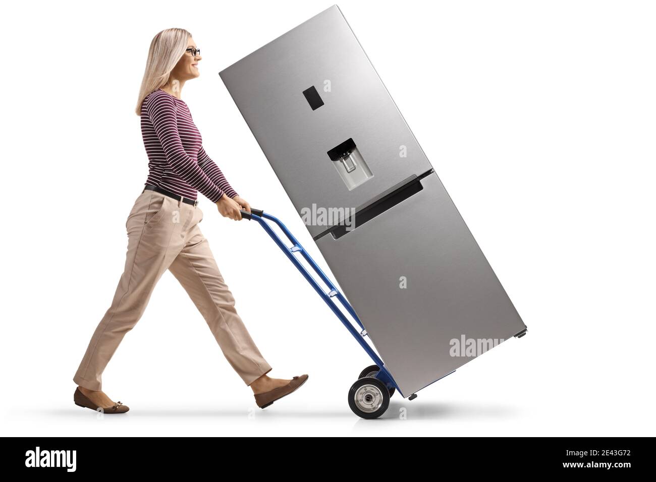Foto di profilo a lunghezza intera di una giovane donna che spinge un carrello a mano con un nuovo frigorifero in argento isolato su sfondo bianco Foto Stock