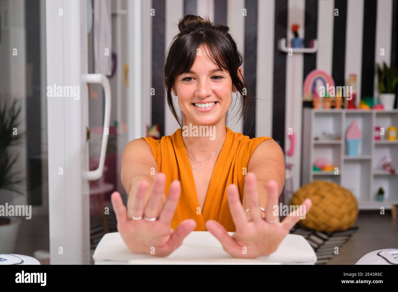 Felice giovane cliente femminile guardando le dita e sorridendo essere felice con manicure perfetto dopo il trattamento in salone di bellezza Foto Stock