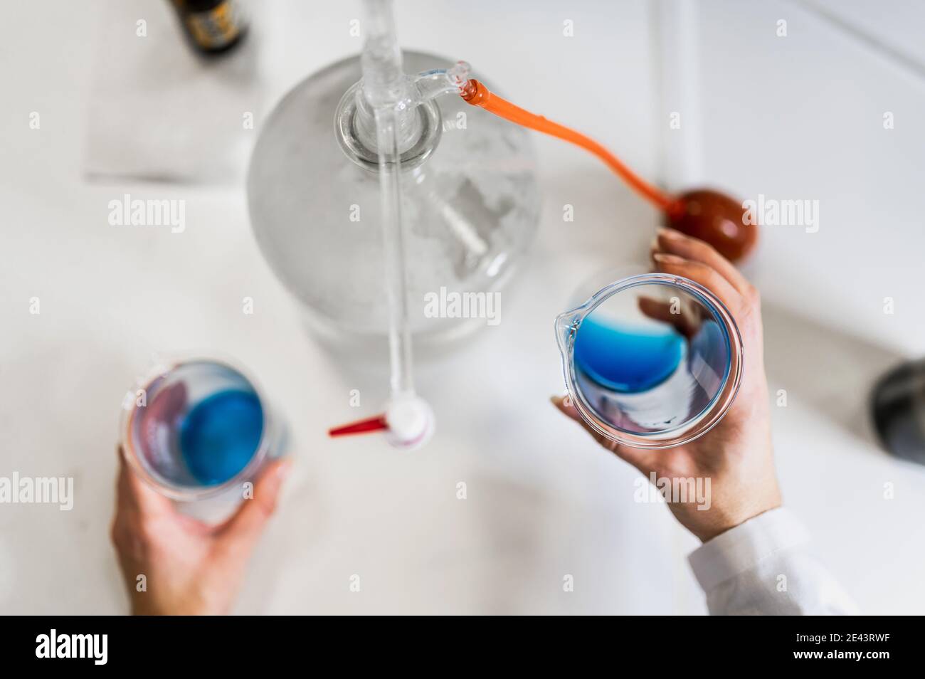 Dall'alto di raccolto anonimo scienziato con becher con blu liquido in mano che conduce esperimenti chimici mentre lavora su nuovo formula per il farmaco Foto Stock