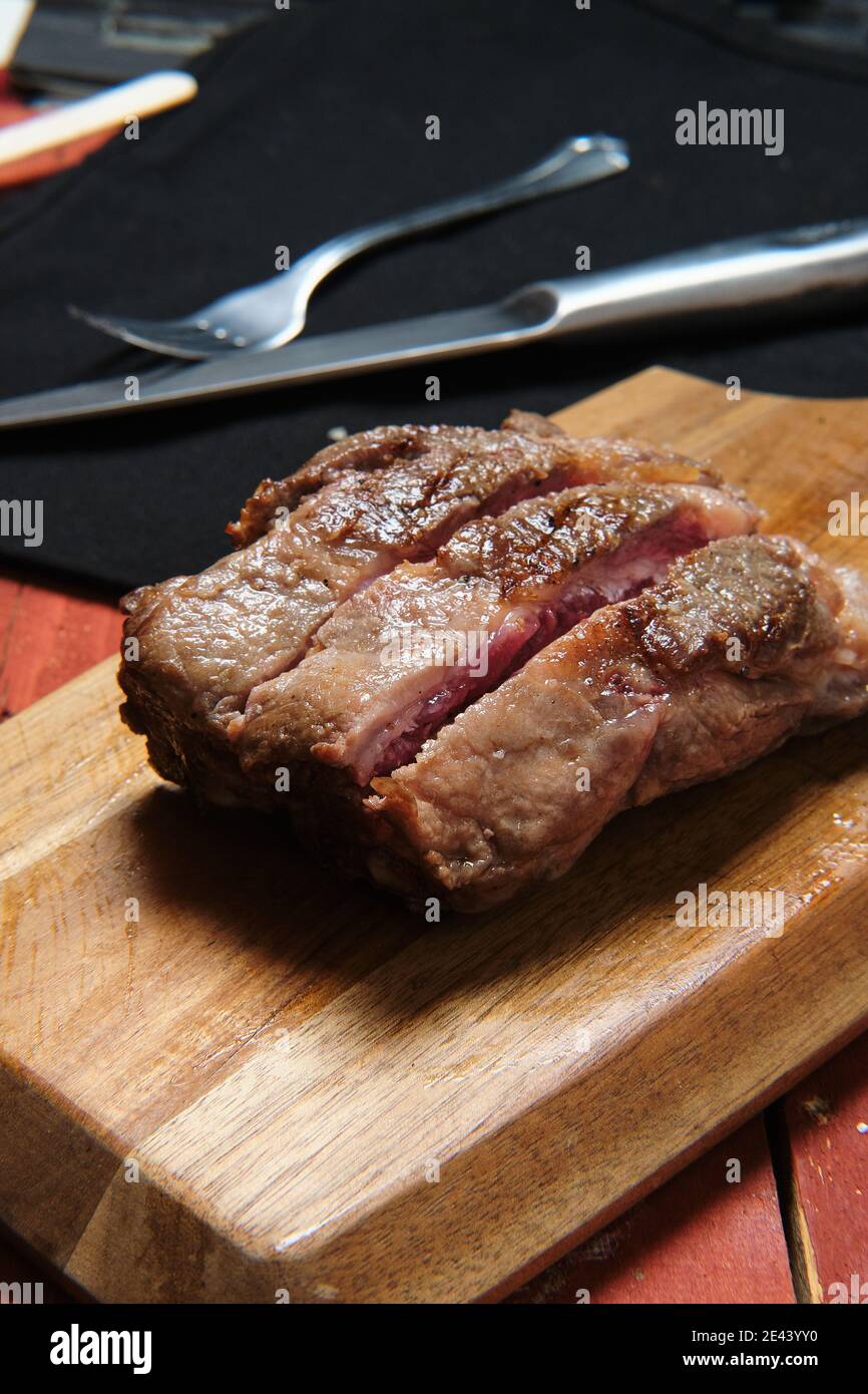 Bistecca di manzo mediamente rara alla griglia servita su tagliere di legno sul tavolo nel caffè Foto Stock