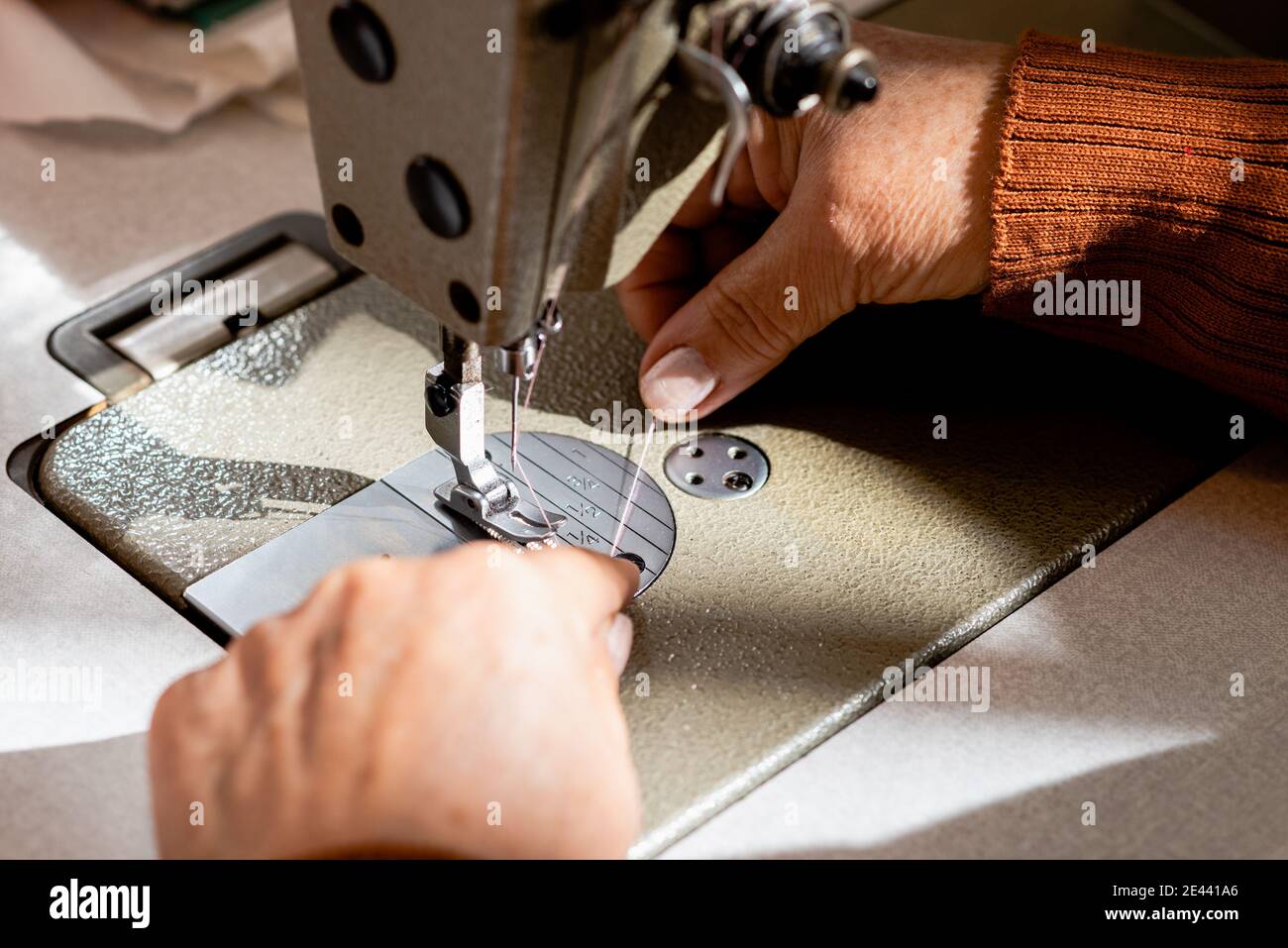 Alto angolo di raccolto seamstress senior senza volto mettendo filo in macchina da cucire in officina Foto Stock