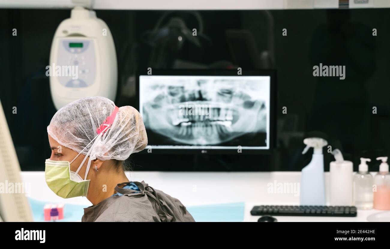 Vista laterale del dentista femminile competente in maschera medica e. Esame uniforme che esegue raggi X dei denti del paziente in clinica moderna Foto Stock