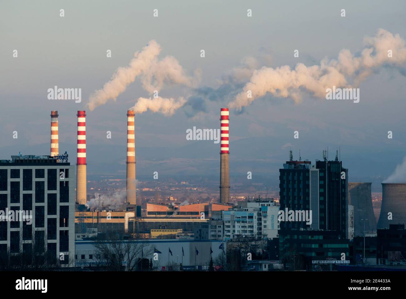 Vista in giustapposizione a contrasto di pile luminose di fumo illuminate dal sole Centrale Termale Est di Sofia Camini fumanti e edifici bui A gennaio 2021 Foto Stock