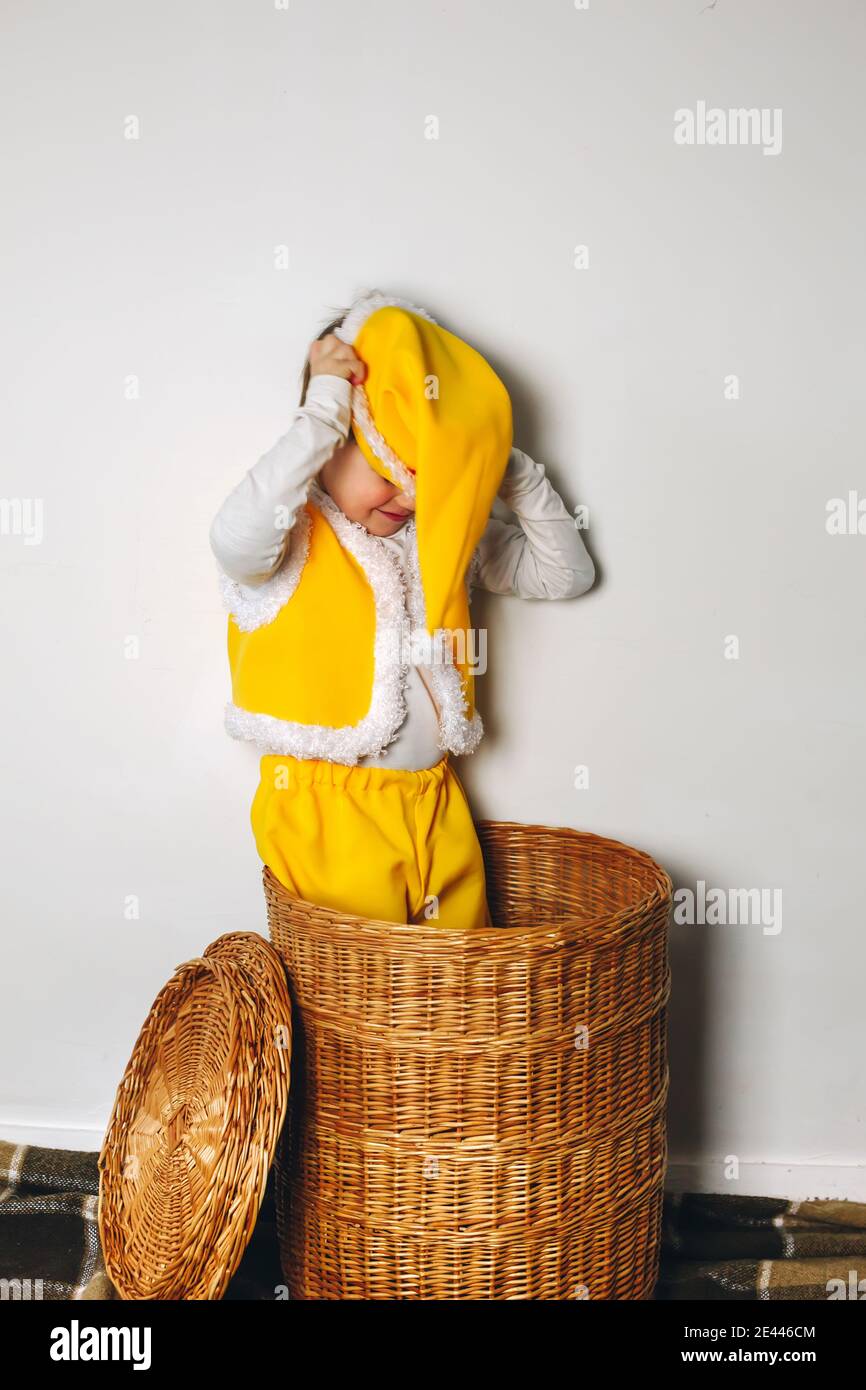 Piccolo ragazzo divertente levarsi in piedi in su dal cestino di paglia e portare il cappello giallo del gnome dell'elfo, divertimento felice della famiglia dell'inverno a casa Foto Stock