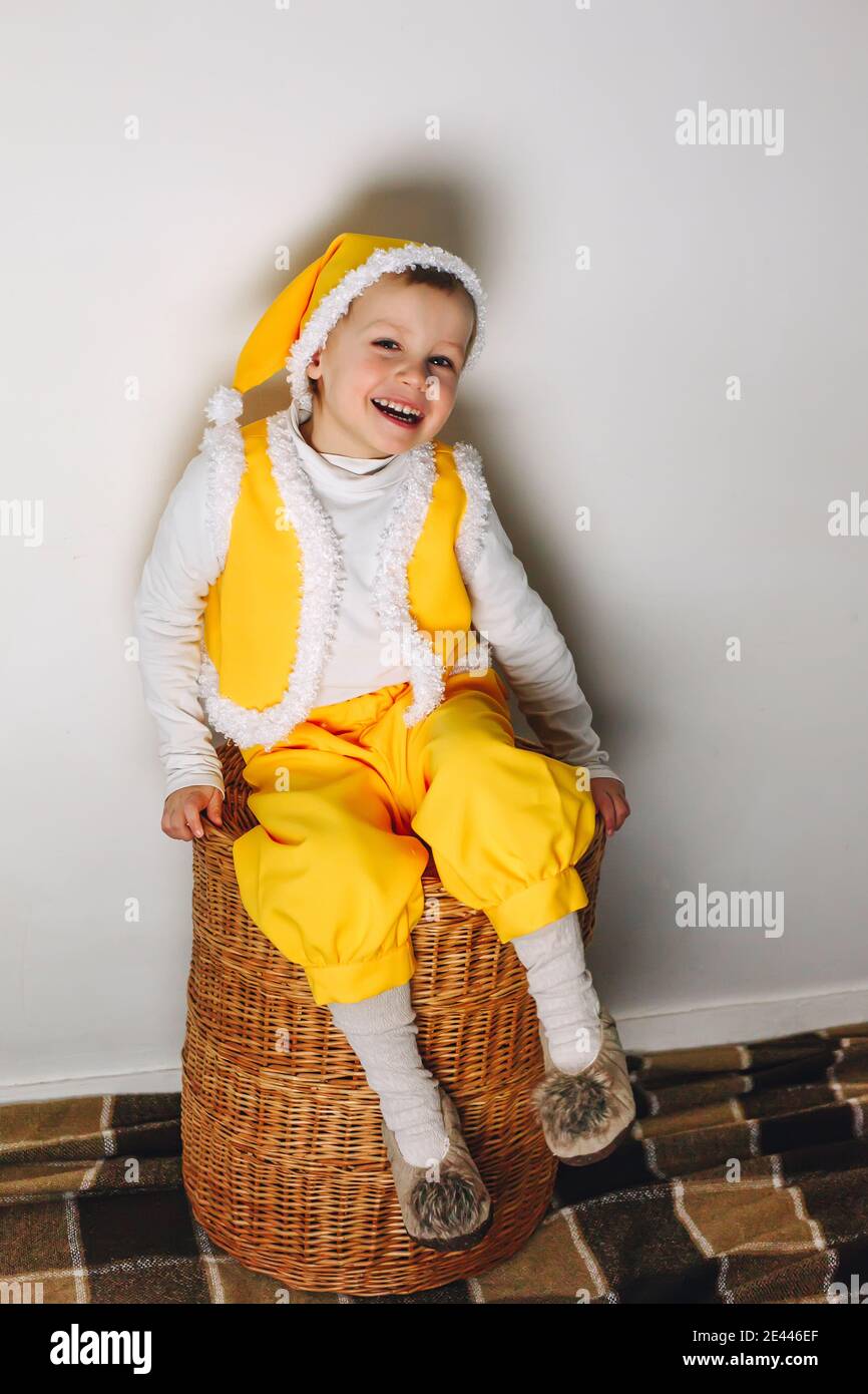 Piccolo ragazzo di 4 anni siediti su cestino di paglia in abito giallo gnome elfo, tempo di casa famiglia invernale Foto Stock