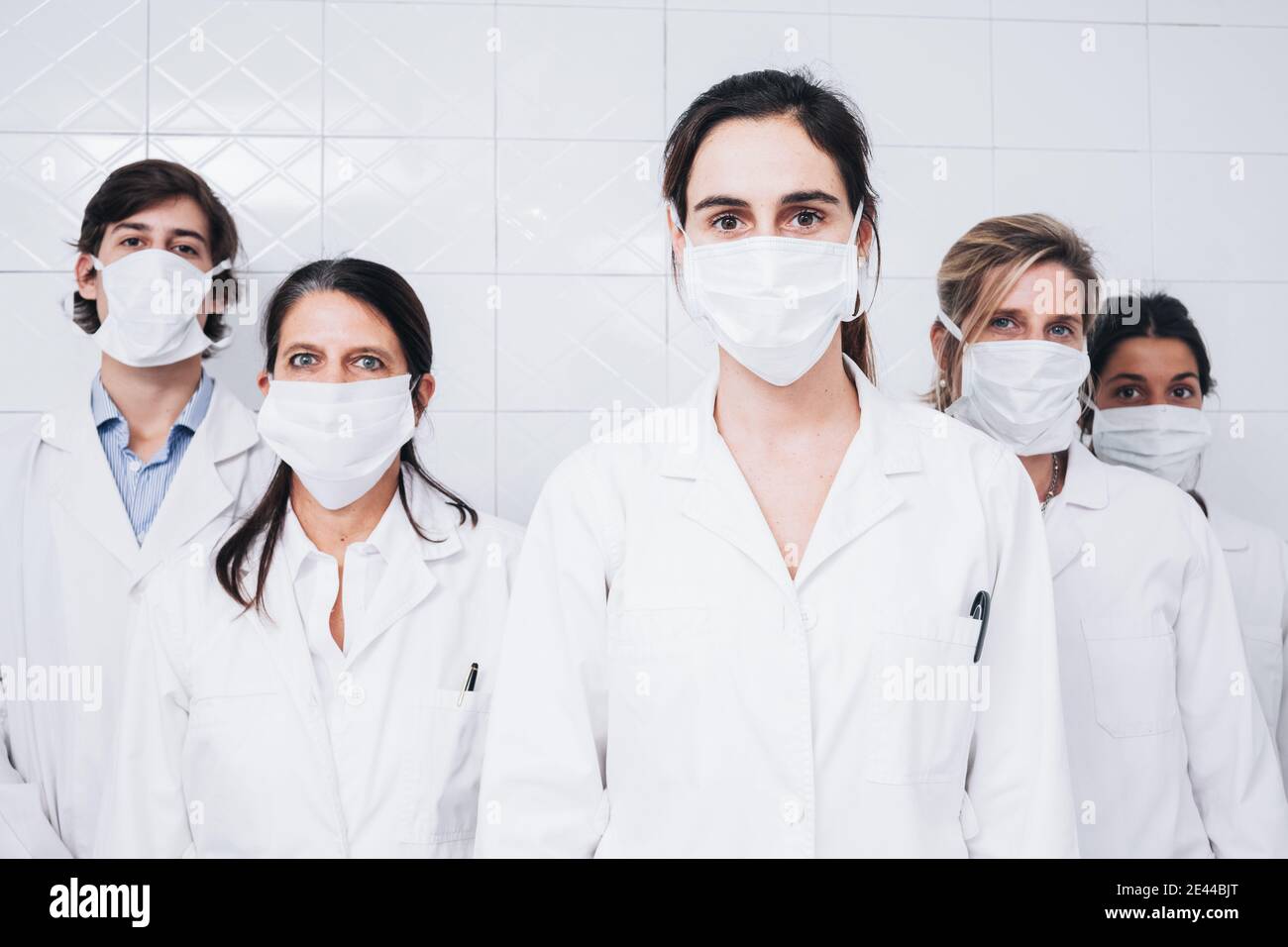 Un gruppo di cinque medici con una maschera sul loro faccia e un cappotto bianco che si alza e si affaccia su fotocamera in una stanza dell'ospedale Foto Stock