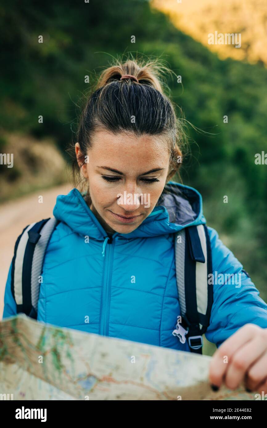 Donna escursionista in abiti caldi in piedi in natura e orientando con mappa cartacea durante il trekking Foto Stock