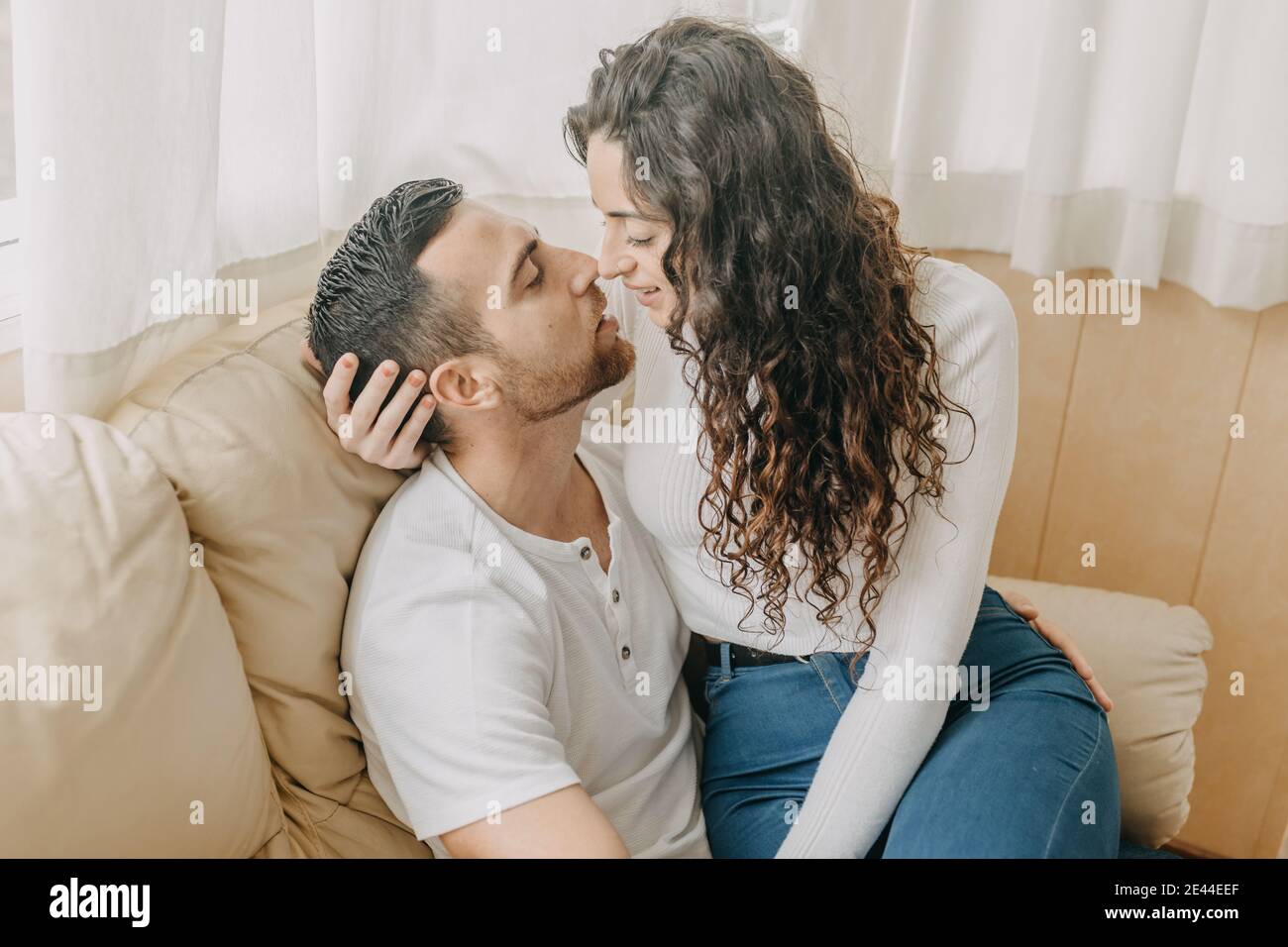 Coppia amorevole seduta su morbido divano e teneramente abbracciando mentre goditi il weekend insieme a casa tua Foto Stock