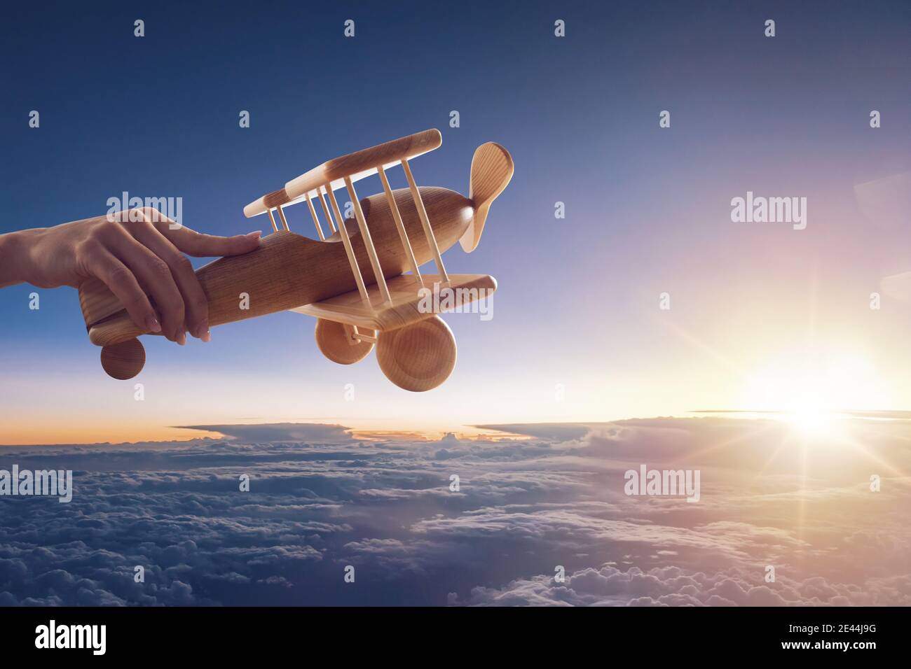 Primo piano di un aeroplano giocattolo vintage in legno, tenuto da una mano, che vola sopra le nuvole nel cielo Foto Stock