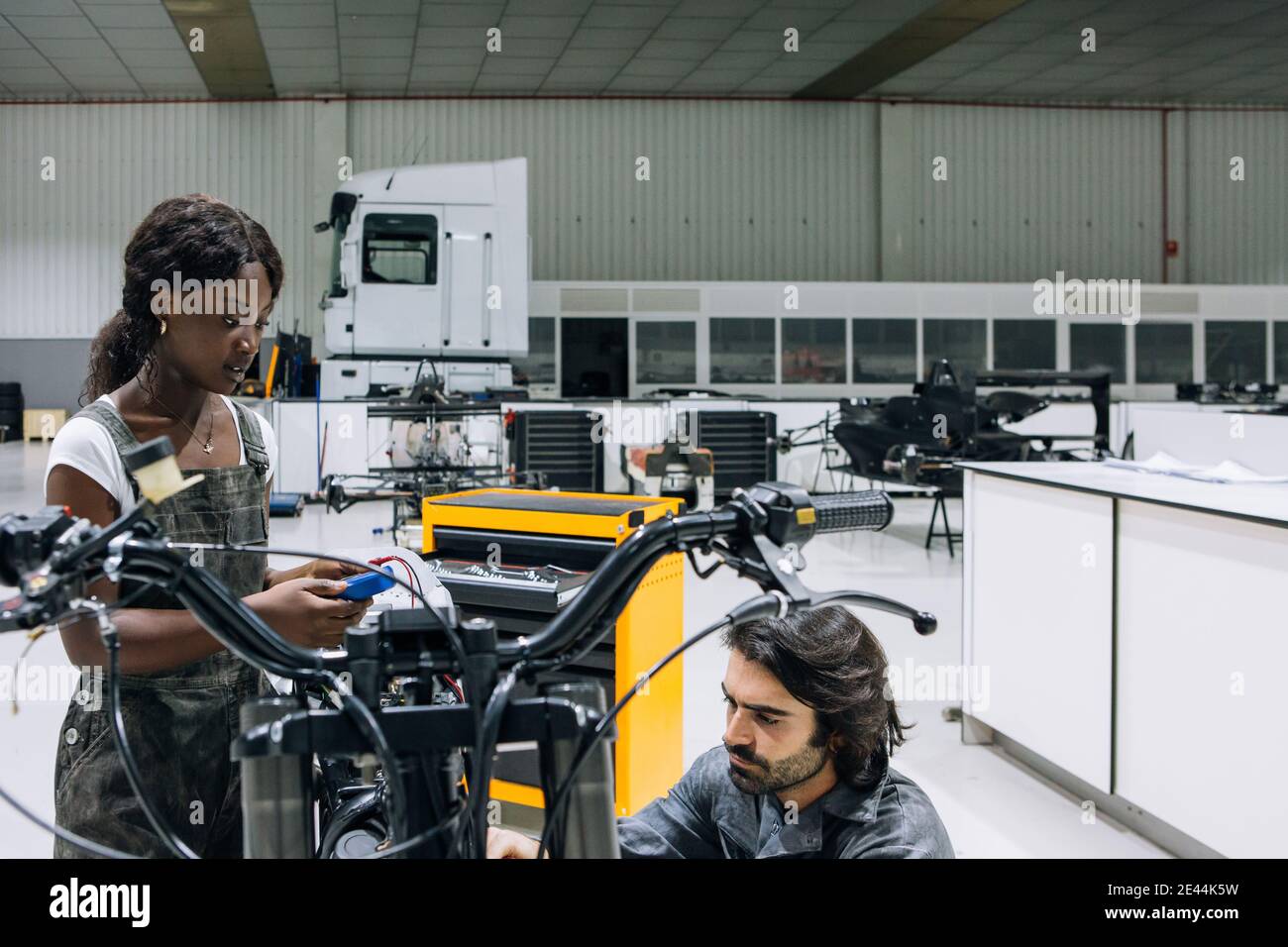 Diversi meccanici maschili e femminili nell'abbigliamento da lavoro che fissano la motocicletta insieme in garage luminoso Foto Stock