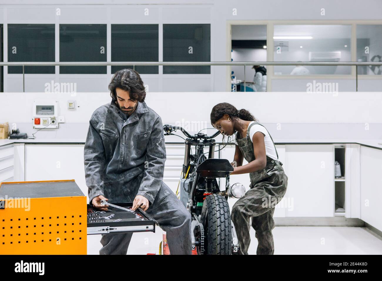 Impegnati tecnici multietnici di sesso maschile e femminile nel fissaggio di indumenti da lavoro sporchi motocicletta mentre si utilizzano strumenti dall'armadietto portautensili Foto Stock