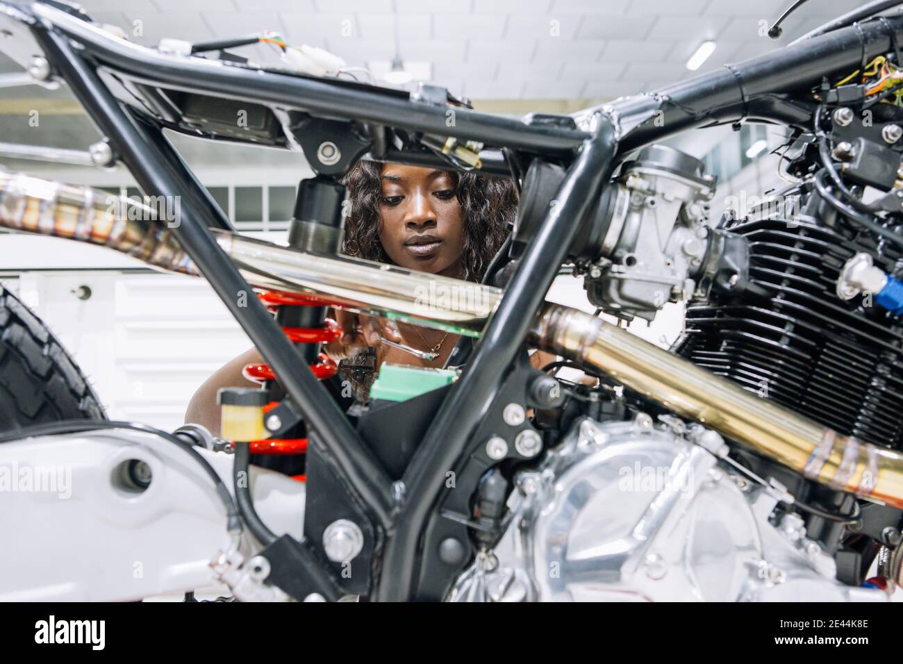 African American femmina meccanico con chiave fissa moto personalizzato mentre lavori in officina Foto Stock