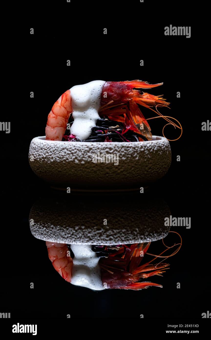 Delizioso piatto con gamberi e ricci di mare servito in ciotola con salsa bianca e posto su tavola specchiata in molecolare ristorante gastronomico Foto Stock