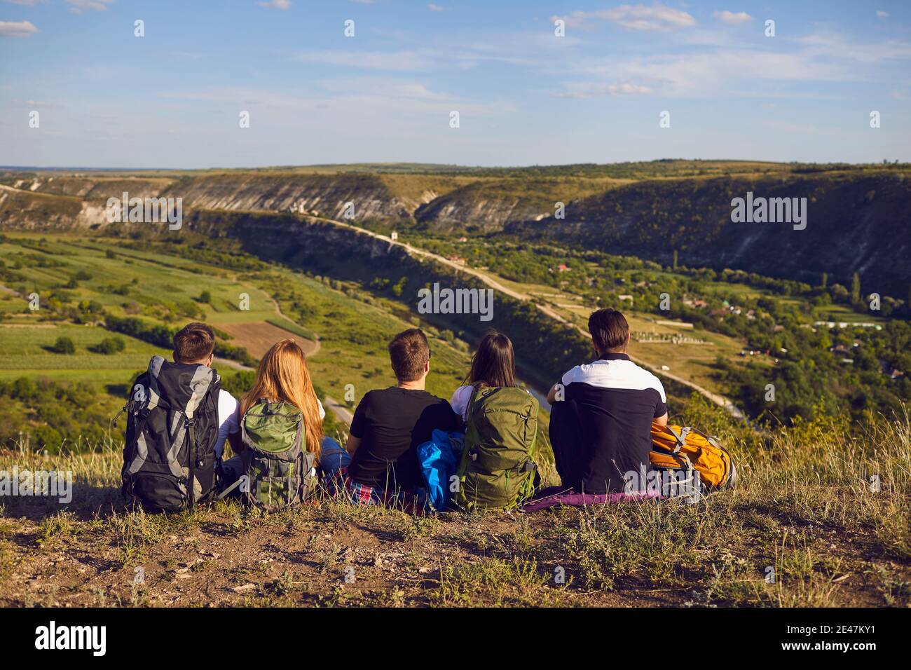 Sognante gruppo di giovani escursionisti seduti sul bordo della montagna e guardando in lontananza. Foto Stock