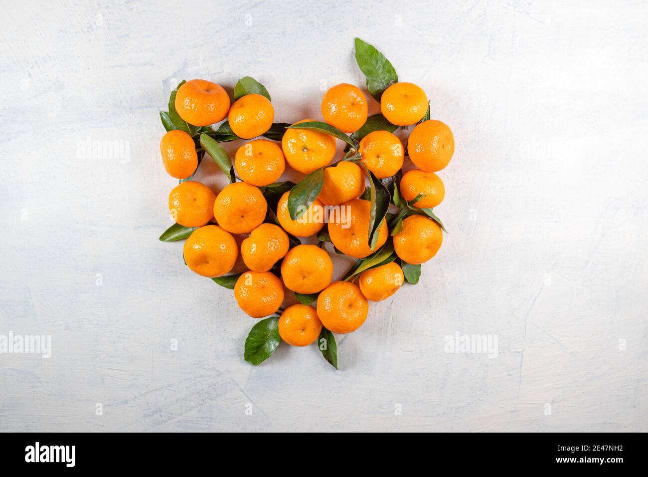 Tangerini arancioni con foglie verdi a forma di cuore su fondo di pietra bianca. Cuore fatto da tangerini. Vista dall'alto. Spazio di copia. In alto Foto Stock