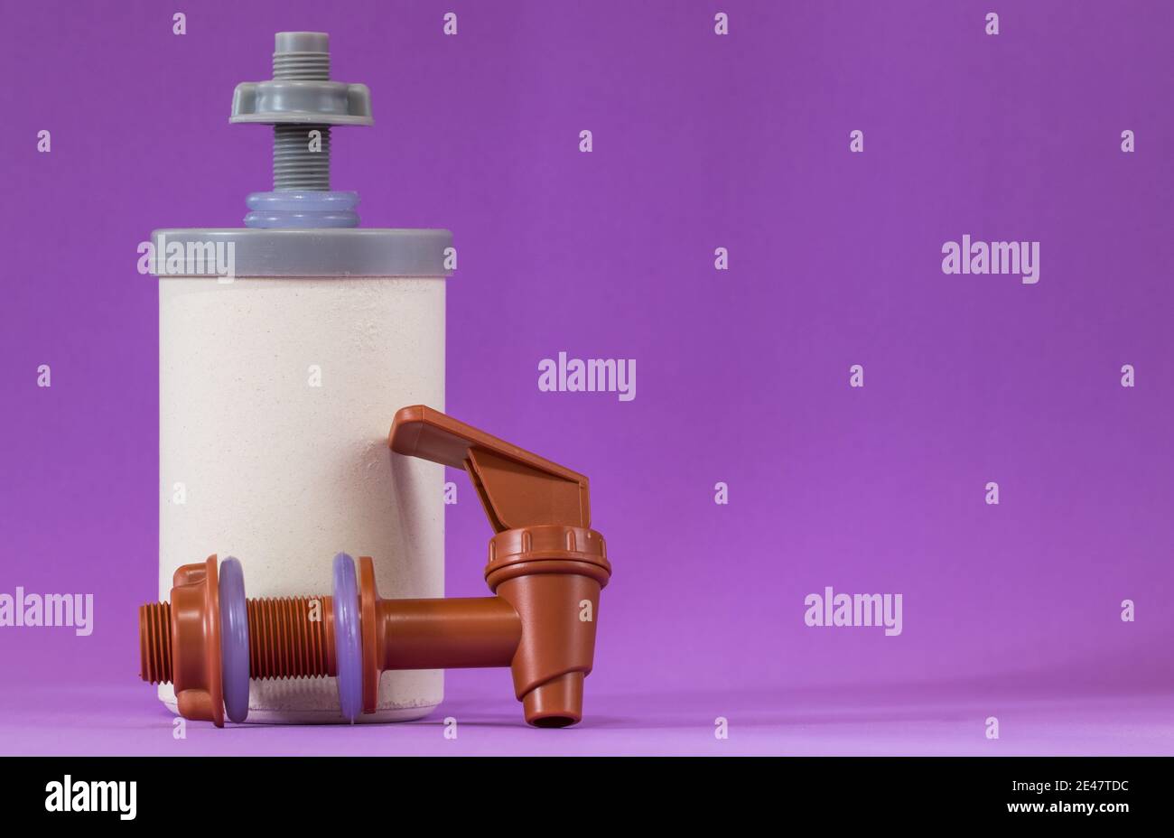 Primo piano dell'elemento filtrante dell'acqua in plastica e del rubinetto in plastica su sfondo viola Foto Stock