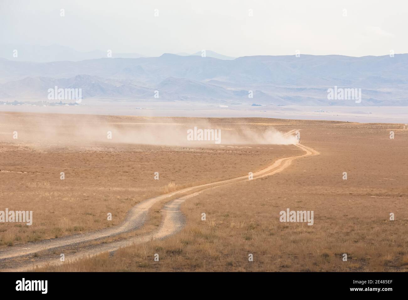 Un veicolo lontano parte dietro un sentiero di polvere su una strada sterrata vuota nel Parco Nazionale del Charyn Canyon nella provincia di Almaty del Kazakistan. Foto Stock