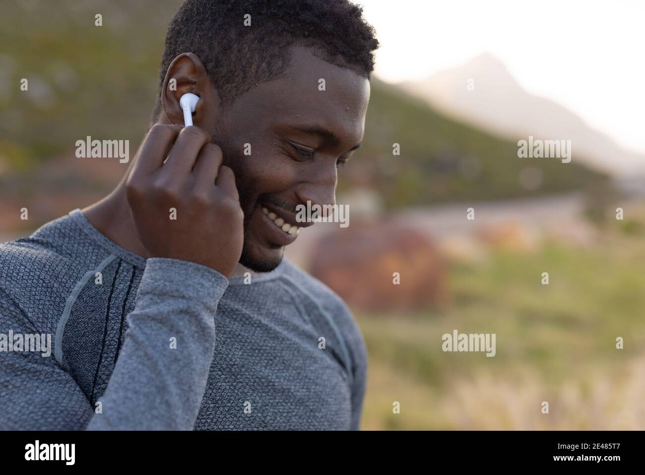 Ritratto di uomo afro-americano in vestiario sportivo indossando gli auricolari in in erba alta Foto Stock