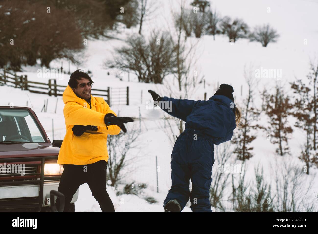 Due amici che lottano con palle di neve nella neve con il auto 4wd sullo sfondo Foto Stock