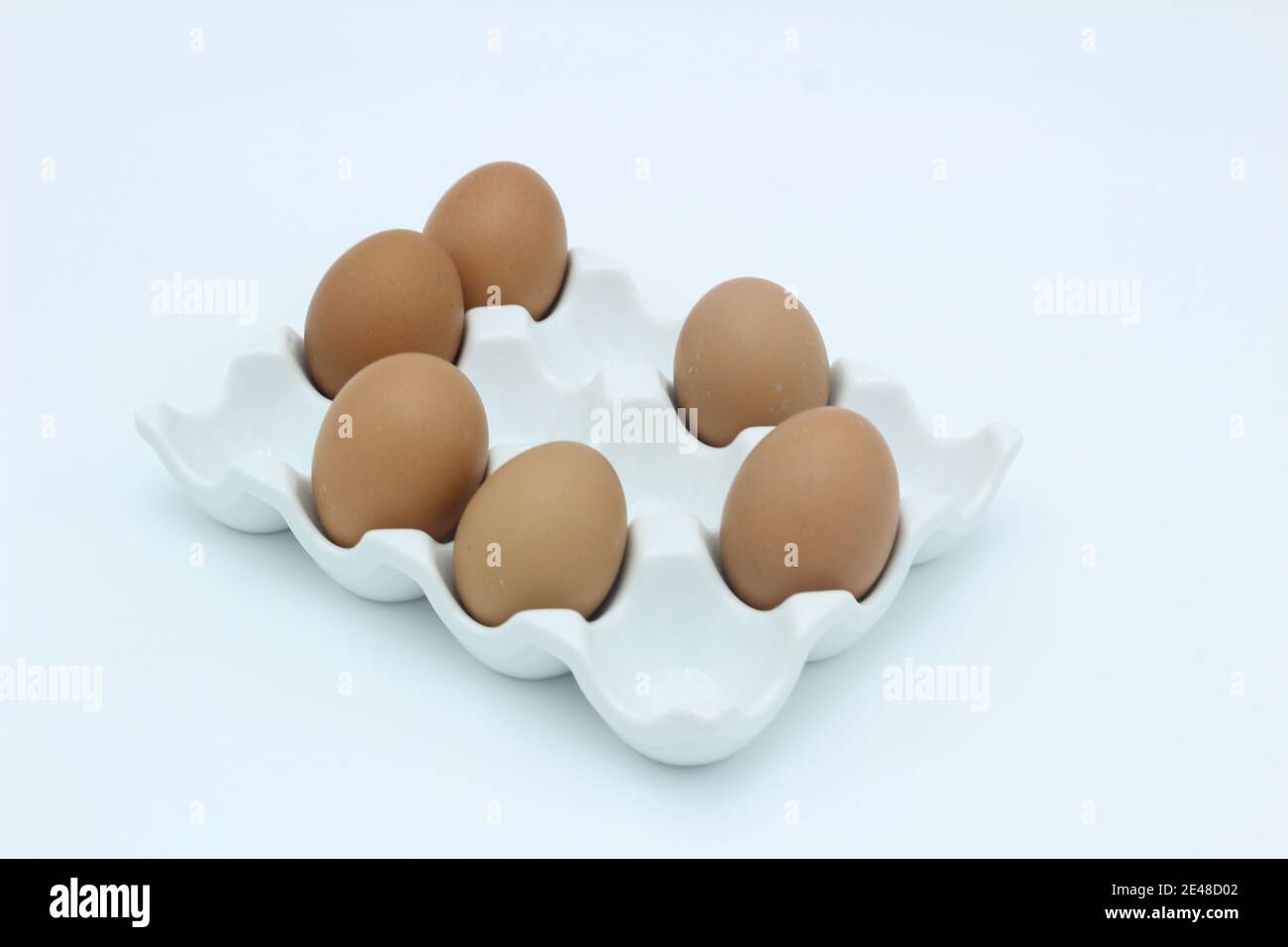 Sei uova di colore marrone in un rack di uovo contro uno sfondo bianco Foto Stock
