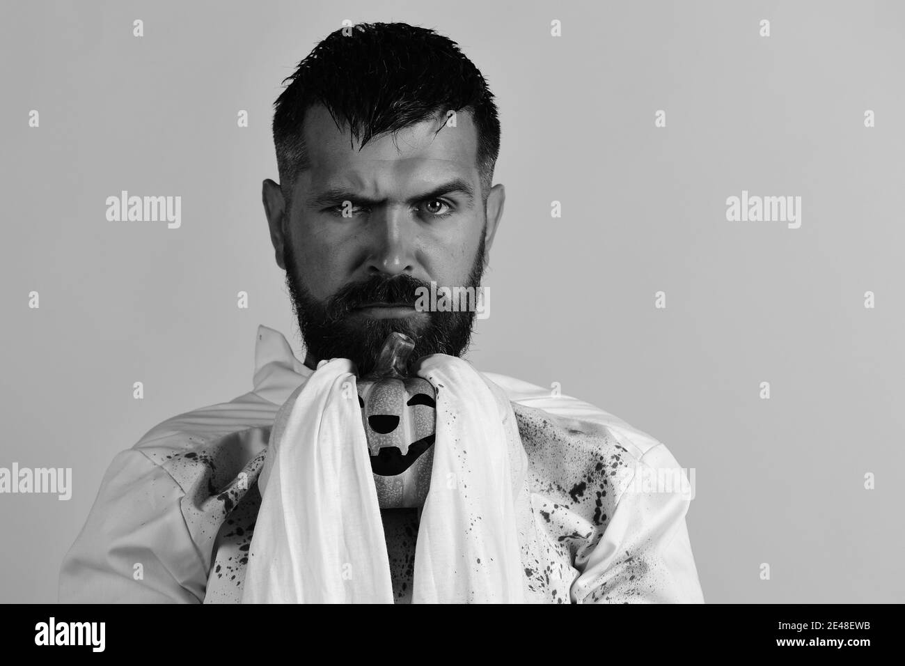 Uomo con faccia grave isolato su sfondo giallo, copia spazio. Il ragazzo con la barba trattiene la zucca arancione. Halloween e concetto di vacanza felice. Personaggio di Halloween in costume fantasma bianco a maniche lunghe. Foto Stock