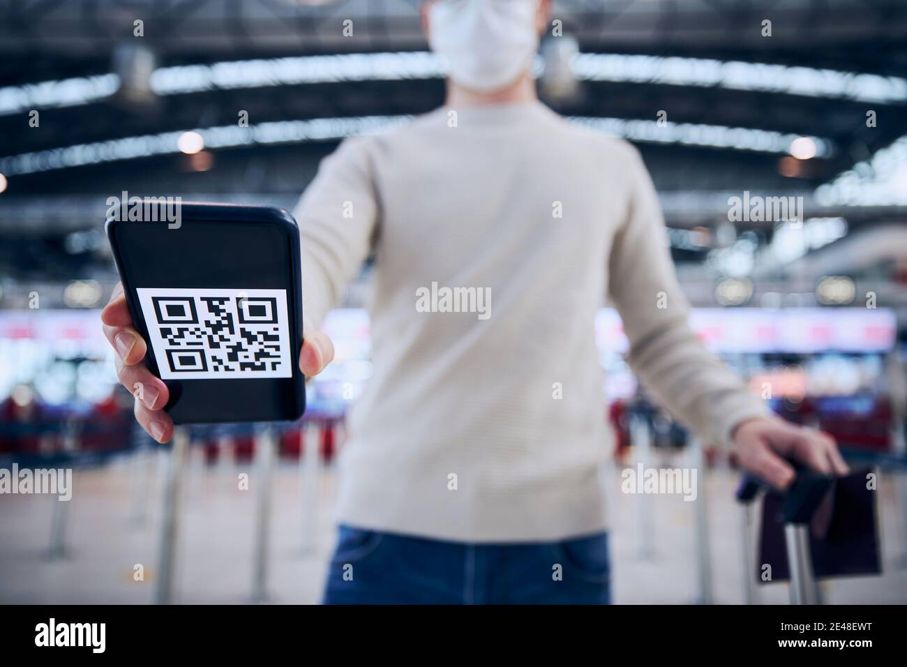 Viaggiare in condizioni normali nuove. Uomo che indossa la maschera facciale e tiene in mano uno smartphone con codice QR all'aeroporto. Temi verifica dell'immunizzazione dopo la vaccinazione WIT Foto Stock