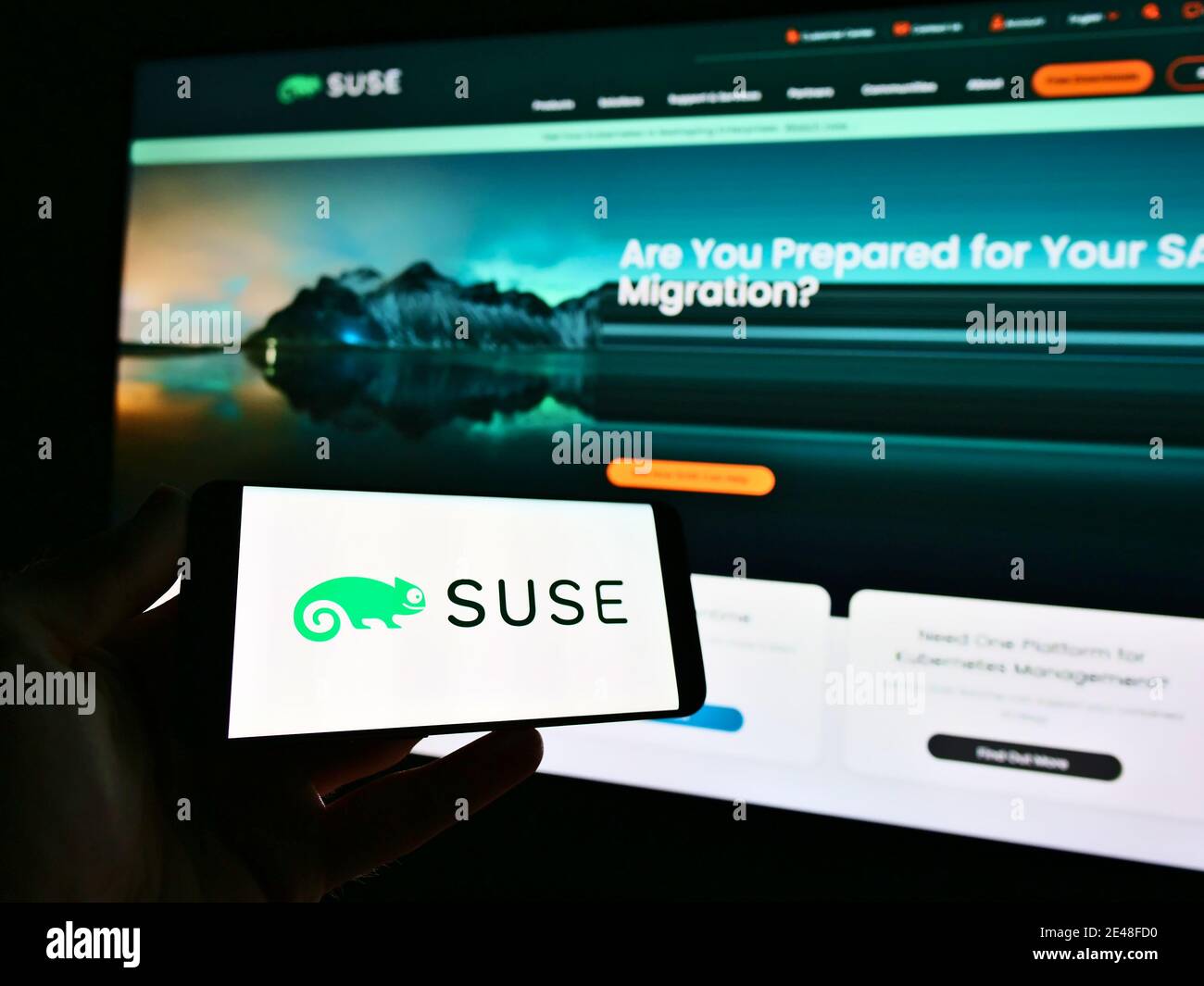 Persona in possesso di smartphone con il logo dello sviluppatore di software tedesco SUSE Software Solutions Germany GmbH in esposizione. Mettere a fuoco sulla sinistra dello schermo del telefono. Foto Stock