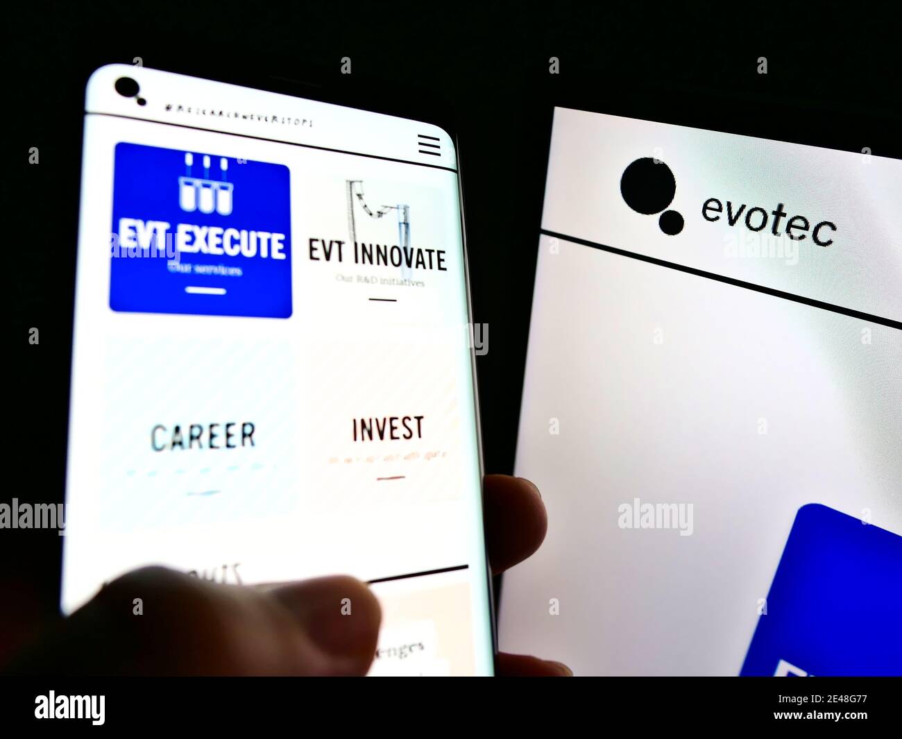 Persona che tiene smartphone con il sito web della società tedesca di biotecnologia Evotec se oltre computer monitor. Concentratevi sul logo aziendale sullo schermo destro. Foto Stock