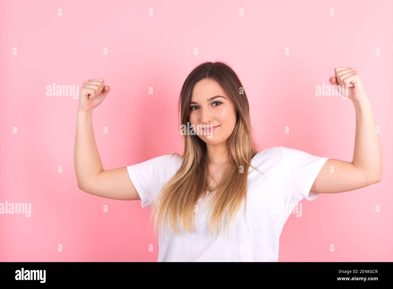 Splendida giovane donna forte isolata su parete rosa di fondo mostrando bicipiti. Potenza della ragazza Foto Stock