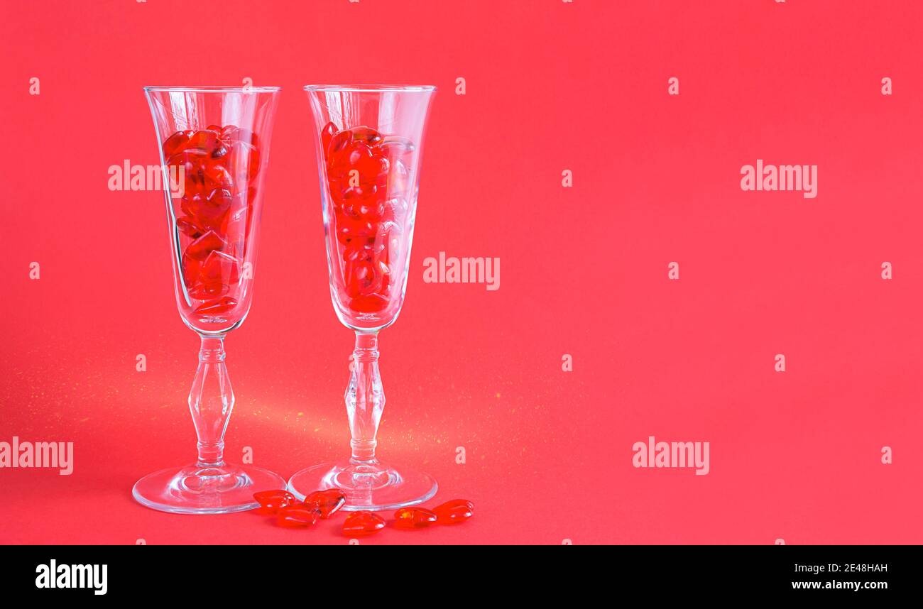 Due bicchieri di champagne sono riempiti di cuori di vetro su uno sfondo rosso con spazio per il testo. San Valentino, amore, appuntamento romantico Foto Stock