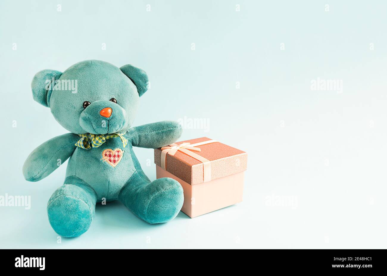 Un morbido orsacchiotto turchese con cuore ricamato contiene una scatola regalo e un prua su sfondo blu. Giocattolo per bambini. Amore, un regalo per le vacanze, un declar Foto Stock