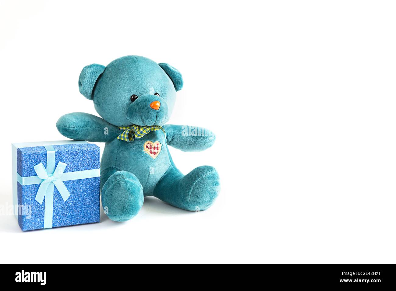 Un morbido orsacchiotto turchese con cuore ricamato contiene una scatola regalo e un prua su sfondo bianco. Giocattolo per bambini. Amore, un regalo per le vacanze, un decla Foto Stock